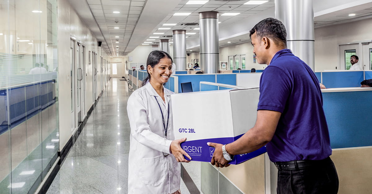 Healthcare worker receiving a temperature-controlled medical shipment from a delivery staff member in a hospital corridor