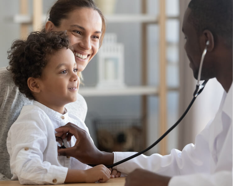 A doctor using a stethoscope on a child held by his mother.